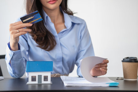 Asian woman with long hair in the blue shirt is using a credit card for buying a new house and looking at home-buying documents The idea of purchasing a home with a credit card.の写真素材