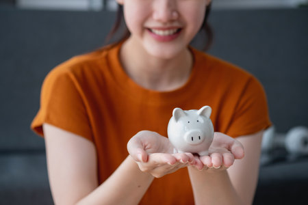 Young Asian woman saving for retirement Saving money through a piggy bank and taking notes on notebook, savings concept.の写真素材