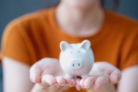 Young Asian woman saving for retirement Saving money through a piggy bank and taking notes on notebook, savings concept.の写真素材