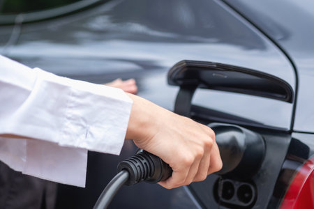 electric car or EV charging station A woman plugs in a black power cable to charge for clean energy for a trip eco concept and clean energy with electric vehicle technology.の写真素材