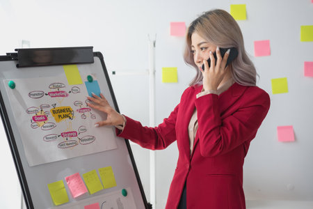 Asian businesswoman presenting a profitable company marketing plan with confidence at the office and future investment plans of the company with charts and graphs on the board.の写真素材