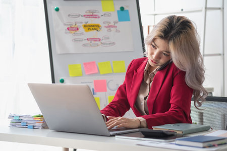 Busy businesswoman at work and talking on the phone looking at laptop screen Frustrated young woman arguing with customer holding a smartphone and being stressed solve business problems.の写真素材