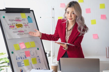 Asian businesswoman presenting a profitable company marketing plan with confidence at the office and future investment plans of the company with charts and graphs on the board.の写真素材