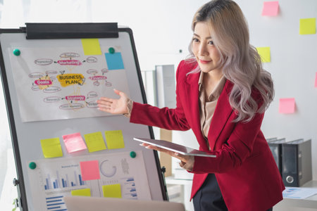Asian businesswoman presenting a profitable company marketing plan with confidence at the office and future investment plans of the company with charts and graphs on the board.の写真素材