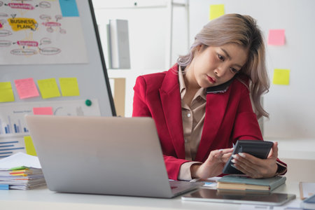Busy businesswoman at work and talking on the phone looking at laptop screen Frustrated young woman arguing with customer holding a smartphone and being stressed solve business problems.の写真素材