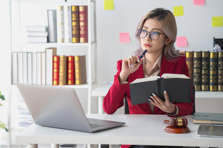 A knowledgeable and confident female lawyer working in an office with law books sitting at the table. Learn, and study, legal services, advice, justice, and real estate concepts.の写真素材
