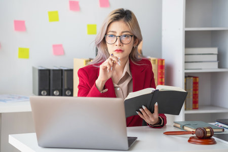 A knowledgeable and confident female lawyer working in an office with law books sitting at the table. Learn, and study, legal services, advice, justice, and real estate concepts.の写真素材