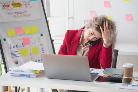 Busy businesswoman at work and talking on the phone looking at laptop screen Frustrated young woman arguing with customer holding a smartphone and being stressed solve business problems.の写真素材