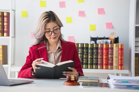 A knowledgeable and confident female lawyer working in an office with law books sitting at the table. Learn, and study, legal services, advice, justice, and real estate concepts.の写真素材