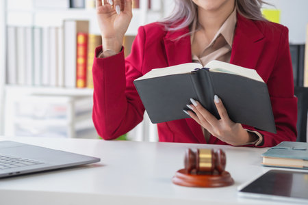 A knowledgeable and confident female lawyer working in an office with law books sitting at the table. Learn, and study, legal services, advice, justice, and real estate concepts.の写真素材