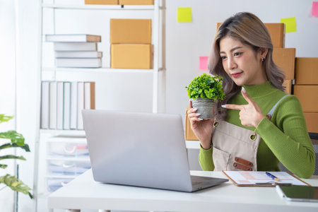 Pretty Asian female blogger reviews products and camcorders on home network, sells online, and presents fake plants on social media. e-commerce business live stream vlogs new normal conceptの写真素材