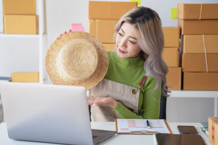 A cute Asian female blogger reviews products and camcorders on a home network, sells online, and presents fashion hats on social media. E-commerce business live stream vlogs new normal concept.の写真素材