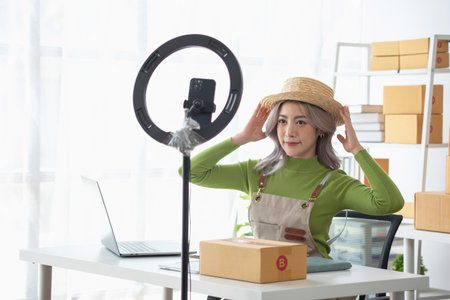 A cute Asian female blogger reviews products and camcorders on a home network, sells online, and presents fashion hats on social media. E-commerce business live stream vlogs new normal concept.の写真素材