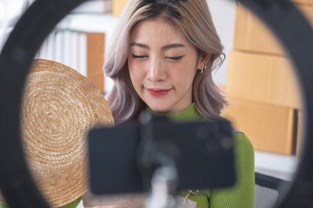 A cute Asian female blogger reviews products and camcorders on a home network, sells online, and presents fashion hats on social media. E-commerce business live stream vlogs new normal concept.の写真素材