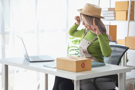A cute Asian female blogger reviews products and camcorders on a home network, sells online, and presents fashion hats on social media. E-commerce business live stream vlogs new normal concept.の写真素材