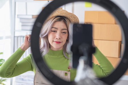 A cute Asian female blogger reviews products and camcorders on a home network, sells online, and presents fashion hats on social media. E-commerce business live stream vlogs new normal concept.の写真素材