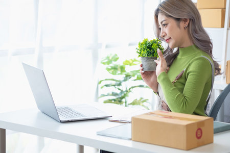 Pretty Asian female blogger reviews products and camcorders on home network, sells online, and presents fake plants on social media. e-commerce business live stream vlogs new normal conceptの写真素材