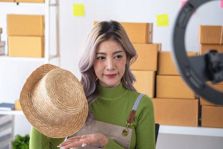 A cute Asian female blogger reviews products and camcorders on a home network, sells online, and presents fashion hats on social media. E-commerce business live stream vlogs new normal concept.の写真素材