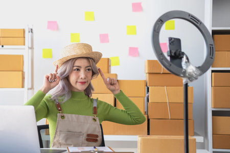 A cute Asian female blogger reviews products and camcorders on a home network, sells online, and presents fashion hats on social media. E-commerce business live stream vlogs new normal concept.の写真素材