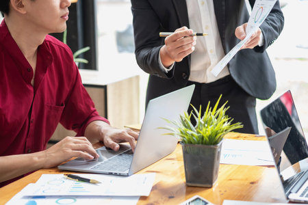Asian business team consists of marketing staff. accountant and financial officer Help each other analyze company profits using tablets. calculator Laptop computers, graph paper, and corporate pens.の写真素材