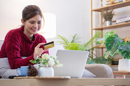 A young Asian woman with a happy smile holds a credit card and uses a smartphone to shop online Online payment concept.の写真素材