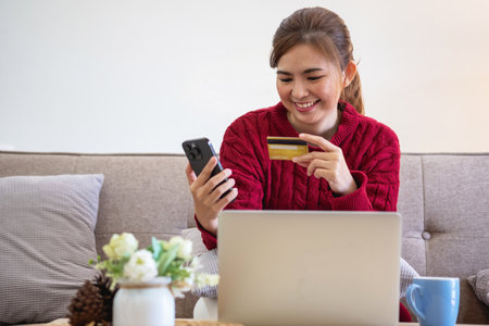 A young Asian woman with a happy smile holds a credit card and uses a smartphone to shop online Online payment concept.の写真素材