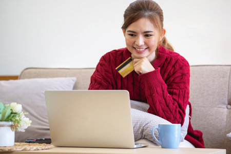 A young Asian woman with a happy smile holds a credit card and uses a smartphone to shop online Online payment concept.の写真素材