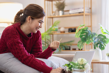 A young Asian woman with a happy smile holds a credit card and uses a smartphone to shop online Online payment concept.の写真素材