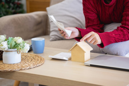 A young Asian woman sits on a sofa in her home, feeling worried and frustrated about her monthly expenses. Various utility bills.の写真素材
