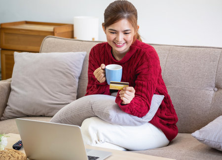 A young Asian woman with a happy smile holds a credit card and uses a smartphone to shop online Online payment concept.の写真素材
