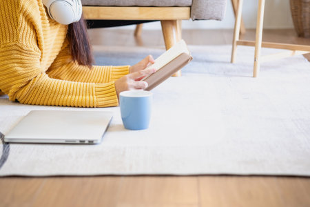 Beautiful young woman in a yellow casual dress enjoying listening to music and smiling while relaxing on the sofa at home. Young woman with headphones uses laptop and smartphone at home. relax conceptの写真素材