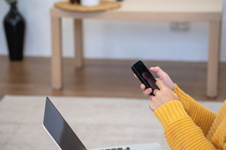 Beautiful young woman in a yellow casual dress enjoying listening to music and smiling while relaxing on the sofa at home. Young woman with headphones uses laptop and smartphone at home. relax conceptの写真素材