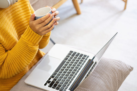 Beautiful young woman in a yellow casual dress enjoying listening to music and smiling while relaxing on the sofa at home. Young woman with headphones uses laptop and smartphone at home. relax conceptの写真素材