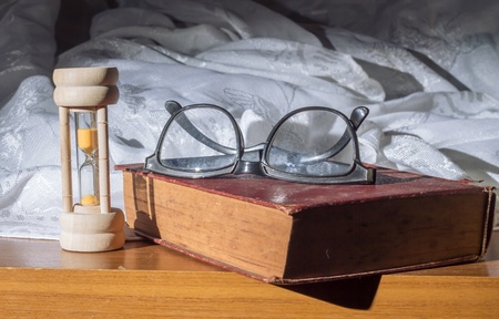 Eyeglass and hour glass with old book の写真素材