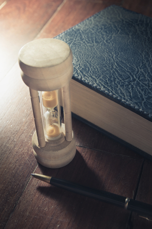 Vintage color filtered hourglass with pen and book.の写真素材