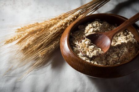 Rolled oats and wheat in wooden bowl with spoonの写真素材