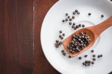 Black peppers on wooden spoon and plate,top view.の写真素材