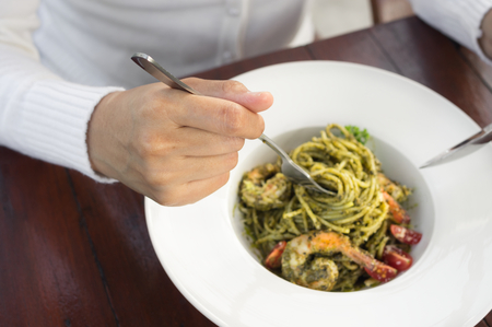 Woman eating green pesto sauce and shrimp spaghetti.の写真素材