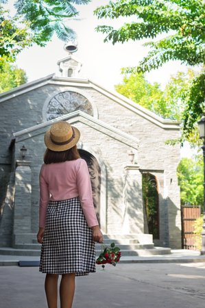 Woman holding flower in hand and standing in front of church.の写真素材