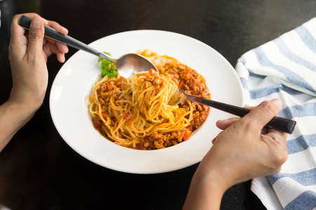 Woman eating spaghetti with tomato sauce in white plate.の写真素材