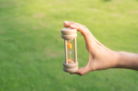 Hour glass in woman hand with green grass background.