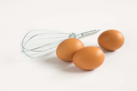 Eggs with metal whisk on white background.の写真素材