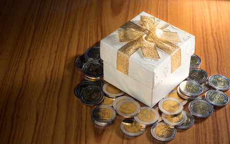 Present box with money coins on table.