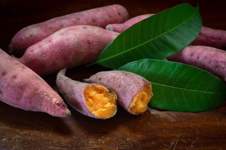 Still life sweet potatoes with green leaves on wooden table.の写真素材