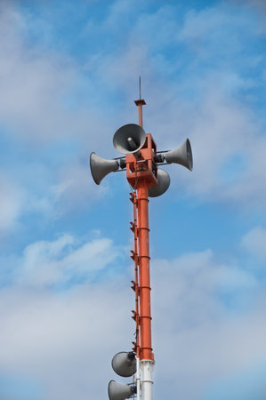 Public loudspeakers on high pole with blue sky.