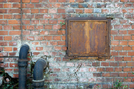 Brick wall of a old house with drainage pipes and one iron windowの写真素材