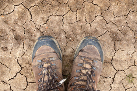 Young man walking the Way of St James, standing in his hiking boots on a dry desert soil in Castilla y León, Spainの写真素材