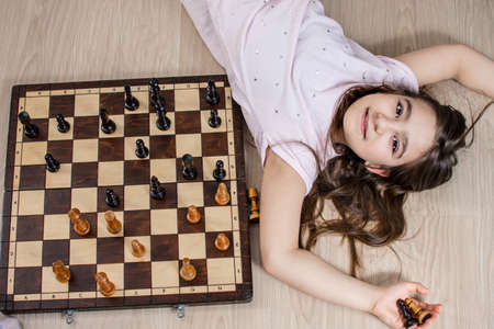 Young girl is lying on the floor and is playing with chess pieces.の写真素材