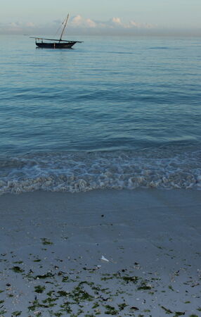 Small waves lapping on the beach with a dhow on the horison