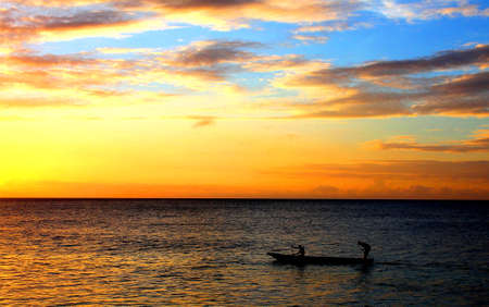 Two people rowing a dugout canoe at sunsetの写真素材